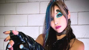 Kairi Sane poses in a black leather top and fingerless gloves with teal glitter eye makeup
