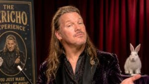 Chris Jericho in a velvet jacket holding a magic wand in front of a red curtain