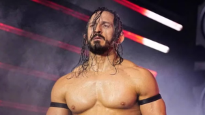 AEW star Pac (Benjamin Satterley) standing under red stage lights with long wet hair and black armbands