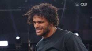 A curly-haired wrestler in a black T-shirt snarls during WWE NXT on The CW