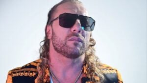 Kenny Omega wearing dark sunglasses and a black-and-gold patterned jacket