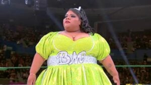 Big Mami stands in the ring in a lime green dress with BM lettering at AAA Héroes Inmortales