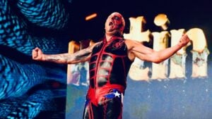 Dustin Rhodes in red and black ring gear and face paint, arms spread during his entrance