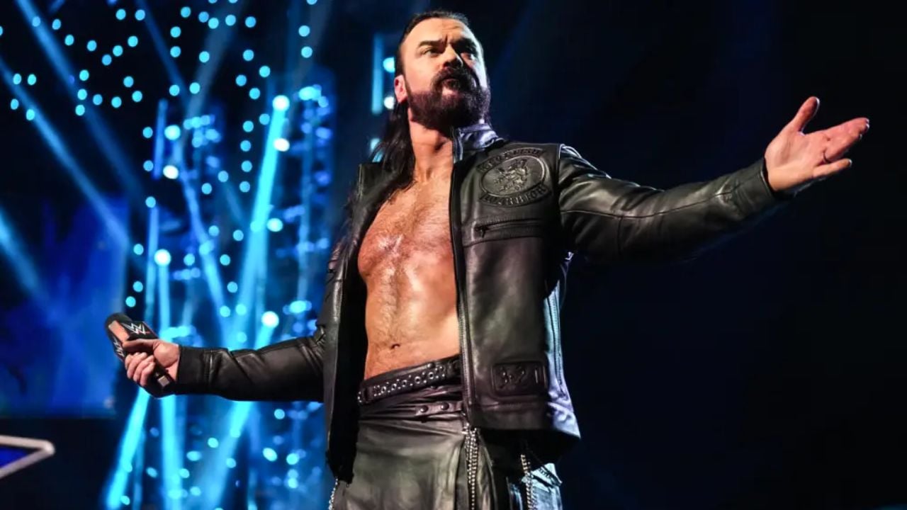 Drew McIntyre holds a microphone with his arms outstretched on a WWE stage