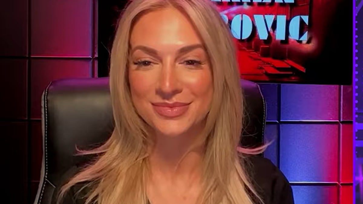 Karmen Petrovic seated during a No Holds Barred interview with colored studio lighting behind her
